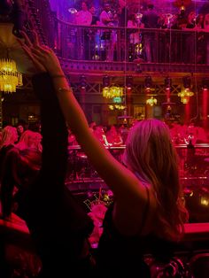 a woman reaching up into the air in front of a crowd at a club or bar