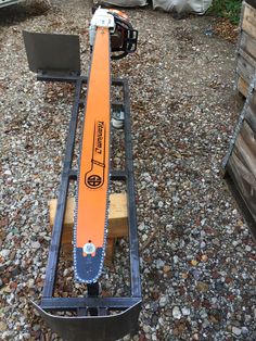 an orange snowboard sitting on top of a piece of metal in the middle of gravel