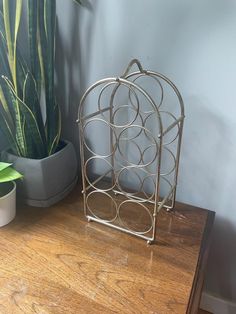 a metal birdcage sitting on top of a wooden table next to a potted plant