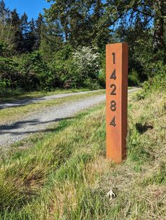 a wooden sign sitting on the side of a dirt road next to a lush green forest