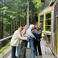 four people hugging each other on a wooden deck in front of a building with yellow windows