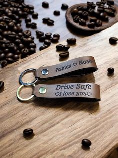 two personalized leather keychains sitting on top of a wooden table next to coffee beans