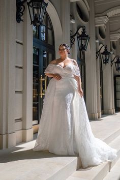 a woman in a white wedding dress standing on some steps with her hand on her hip