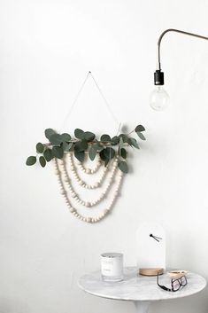 a white table topped with a lamp next to a wall mounted plant and eyeglasses