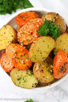 a bowl filled with potatoes and carrots covered in seasoning next to parsley