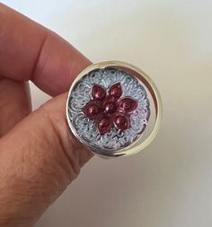 This ring is gorgeous. The Czech glass cabochon measures 18mm (approximately .7"). Looking at the glass straight on you'll see a brilliant, light purple color with a burgundy flower. As you turn it and the light catches it, the purple shifts to a beautiful pink color that's as pretty as the purple color.  The adjustable ring base is silver plated and really sets off the glass cabochon. The front of the ring setting measures approximately 1" x 1".  The last two pictures show what the side and back off the ring setting looks like. Adjustable Pink Flower Ring For Anniversary, Adjustable Round Flower Ring For Anniversary, Adjustable Flower Ring For Anniversary, Nickel Free Adjustable Round Flower Ring, Silver Ruby Ring Gift, Handmade Adjustable Ruby Ring, Red Flower Shaped Rings As Gift, Unique Adjustable Flower Ring, Red Flower Shaped Rings For Gifts