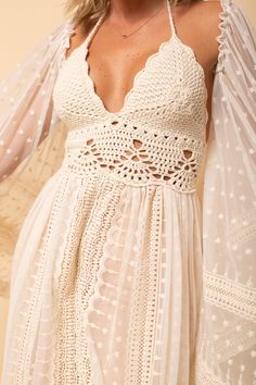 a woman wearing a white dress with sheer sleeves and crochet details on it