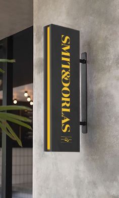 a black and yellow sign hanging on the side of a building next to a potted plant