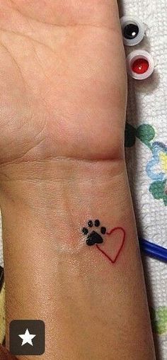 a small wrist tattoo with a dog paw and heart on it's left side