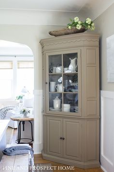 a china cabinet in the corner of a room with white walls and wood flooring