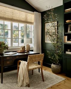 a room with a desk, chair and large window in the corner that has curtains on it