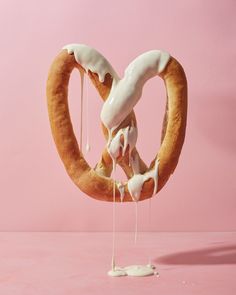 a pretzel being drizzled with icing on a pink background