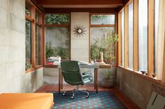 a room with a desk, chair and window on the wall next to an orange couch