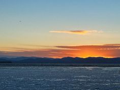 the sun is setting over some mountains and water