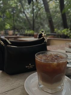 a drink sitting on top of a white plate next to a handbag and purse