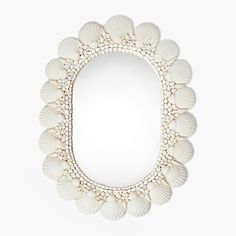 an oval mirror with shells on the bottom and white trimmings, in front of a