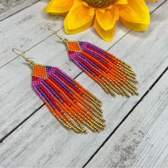 two pairs of beaded earrings sitting on top of a wooden table next to a sunflower