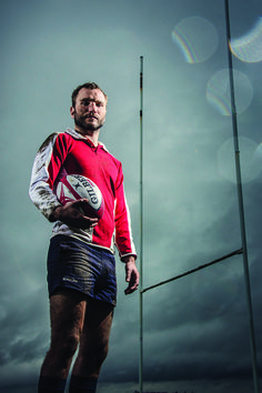 a man holding a rugby ball standing in front of two poles and an american flag