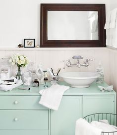 a bathroom sink sitting under a mirror next to a white towel on top of a green dresser