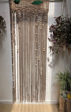 a wall hanging made out of macrame with beads and plants in the background