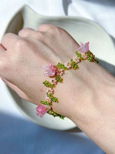 a woman's hand wearing a bracelet with pink flowers and green leaves on it