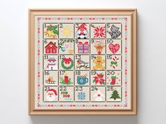 a cross stitch christmas calendar is hanging on the wall in front of a white wall