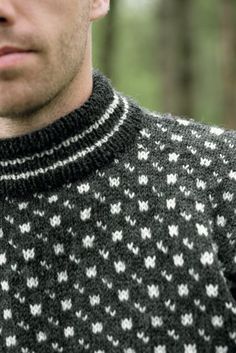 a man wearing a black and white sweater in the woods with his cell phone to his ear