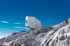 a white box sitting on top of a rocky hill next to a blue sky and clouds