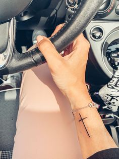 a woman's hand on the steering wheel of a car with a cross tattoo