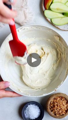 someone is mixing cream in a bowl with apples and other ingredients around it on a table