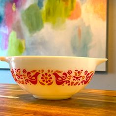 a red and white bowl sitting on top of a wooden table next to a painting