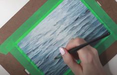 a person is drawing on a piece of paper with a pencil and watercolors