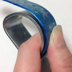 a hand holding a piece of metal with blue paint on it's side and the tip of its finger