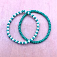 two turquoise and white beaded bracelets sitting on top of a wooden table