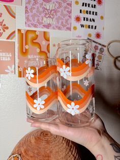 two glasses with orange and white flowers are held in front of a woman's face