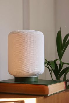 a white lamp sitting on top of a wooden table next to a book and potted plant