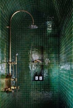 a green tiled bathroom with gold fixtures and shower head in the corner, along with shelves on the wall