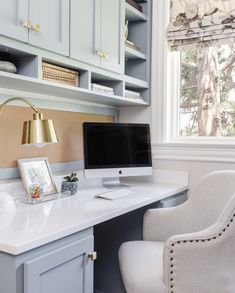 a desk with a computer on top of it next to a chair and lamp in front of a window