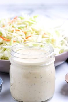 a bowl of coleslaw next to a glass jar filled with dressing