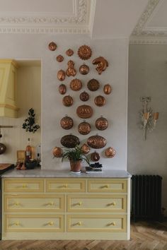 a kitchen with yellow cabinets and lots of gold decorations on the wall, along with a potted plant