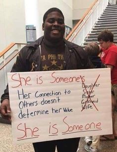 a man holding a sign that says she is someone