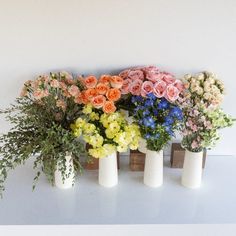 four white vases filled with different colored flowers