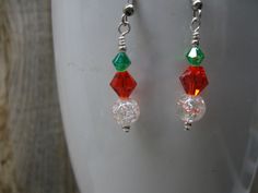 Inspired during the Christmas season these dangle earrings feature a red and green crystal and a clear crackle bead, silver tone beads and silver tone findings.  These earrings would be a great accessory to dress up a casual outfit or wear with jeans and a tee.  From the top of the ear wire to the bottom is approximately 1 3/4" and silicone stops are provided to prevent loss.  The earrings in the photo are the exact pair you will receive.  Designed and handcrafted by me for you in my smoke free studio. No returns accepted but please contact me should there be a problem with your order.   Carefully packaged and shipped in a white box enclosed in a bubble envelope.  Free shipping is USPS First Class Package with tracking.  Expected delivery is 2-6 days. Green Beads, Green Crystal, Bubble Envelopes, White Box, Wire Earrings, Christmas Jewelry, Green Crystals, Green Bead, Christmas Season