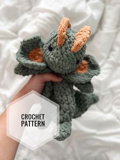 a crochet dragon stuffed animal being held by someone's hand with the words crochet pattern below it