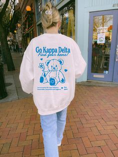 a woman is walking down the street with a teddy bear on her back, wearing a sweatshirt that says go kappa delta