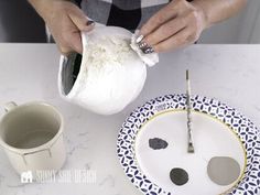 a person is pouring something into a bowl on a plate with two cups and spoons