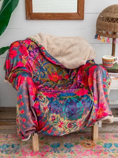 a colorful chair with a blanket on top of it in front of a mirror and potted plant