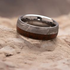 a wedding ring sitting on top of a rock covered in sand and wood grains