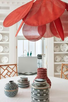 a white table topped with vases covered in red paper flowers and hanging from the ceiling