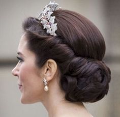 a woman wearing a tiara and smiling at another woman with her hair in a bun